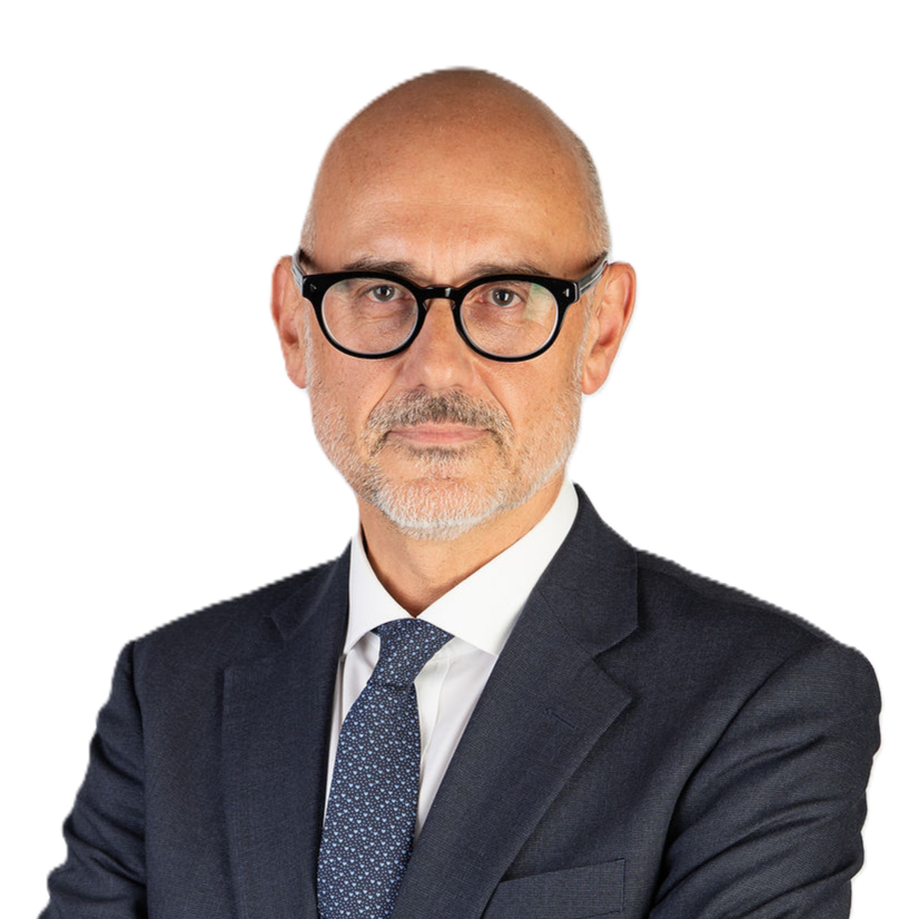 A bald man in a navy suit and tie stands with his arms crossed, looking at the camera.